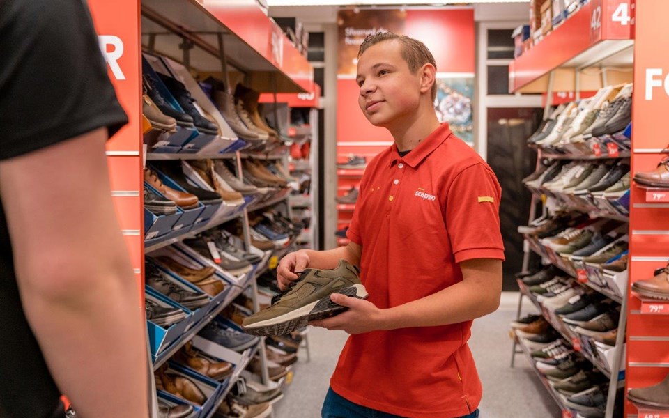 Jongens laat schoen zien aan klant in winkel.
