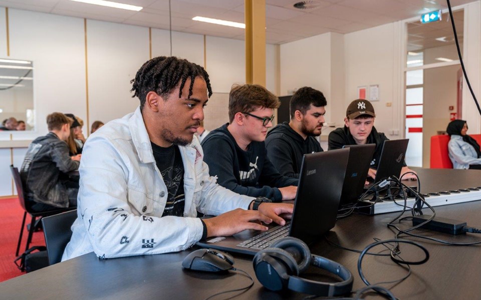 Vier studenten Software Developer zitten naast elkaar aan grote tafels met laptop